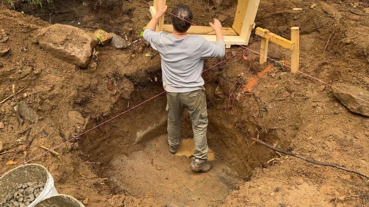 Lowering the footing box into the hole. A little bit of light rain doesn’t stop the progression. Using a plumb bob to mark centre and figure…